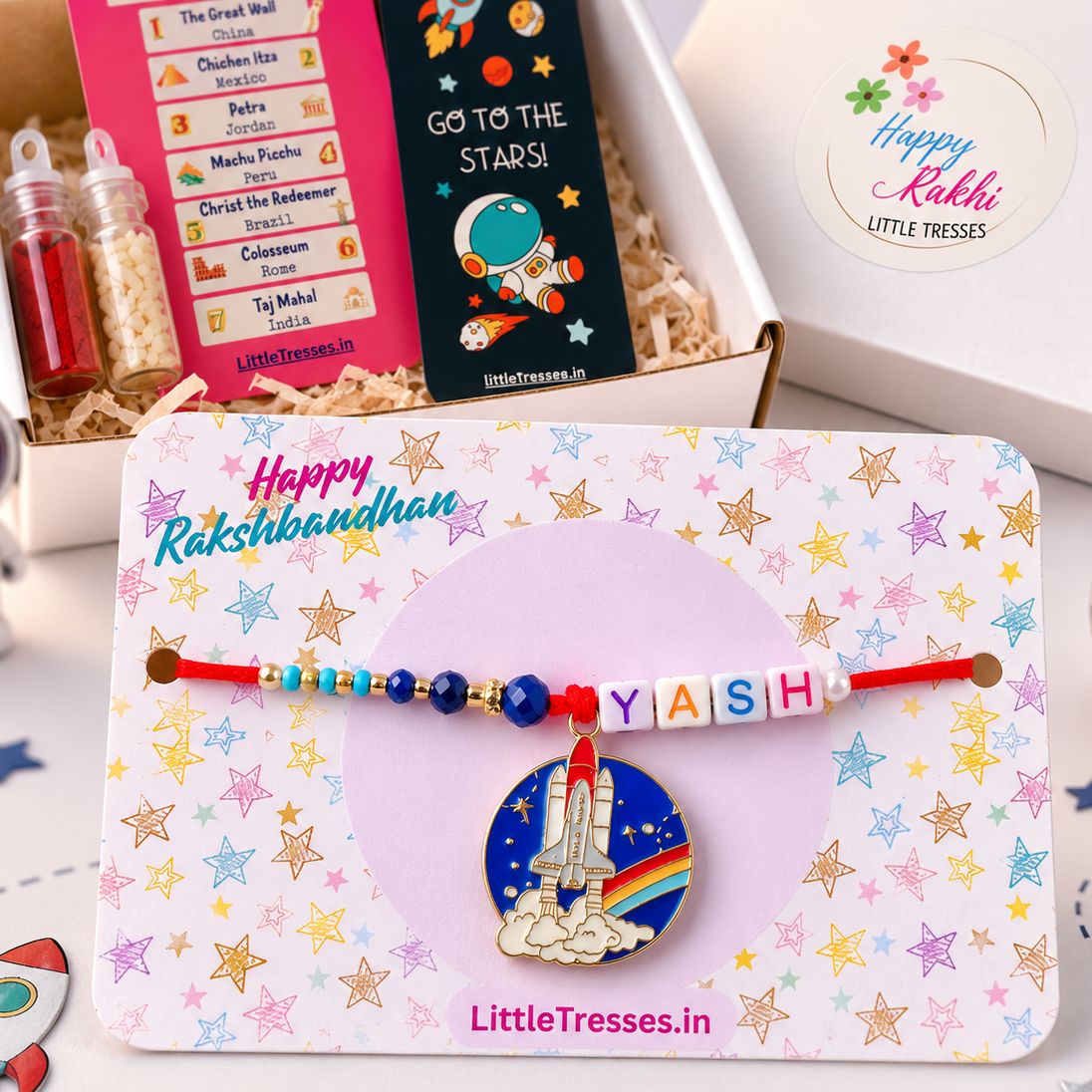Celebrate Raksha Bandhan with the Little Tresses Personalized Space Enthusiast Bro Rakhi Gift Box. Features a custom name rocket-themed Rakhi with activity cards, greeting card, roli bottle and rice bottle in a premium gift-ready box.